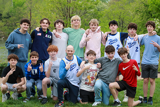 A diverse group of young adults jumping with excitement in a lush green garden during a community event.